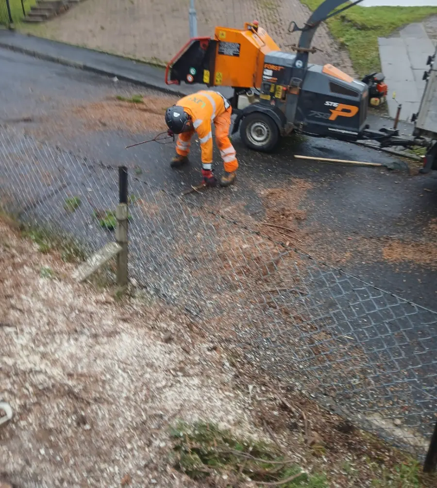 A team member in orange picking up the last branches from the road beside the wood chipper