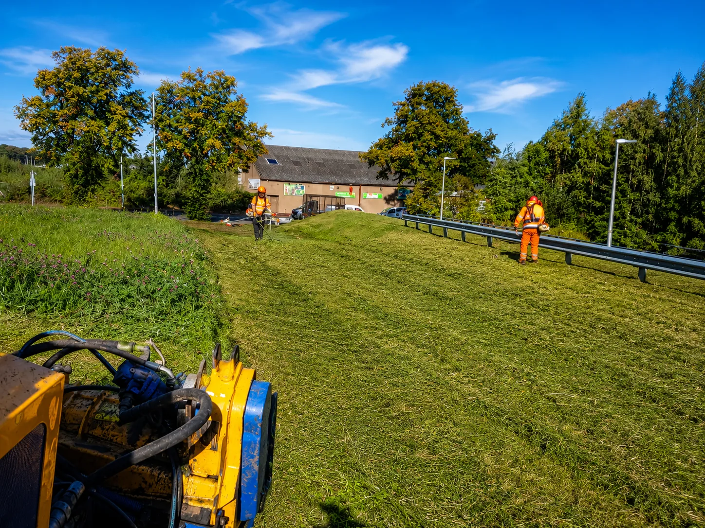 Robo flail and operatives clearing vegetation on a steep roadside embankment